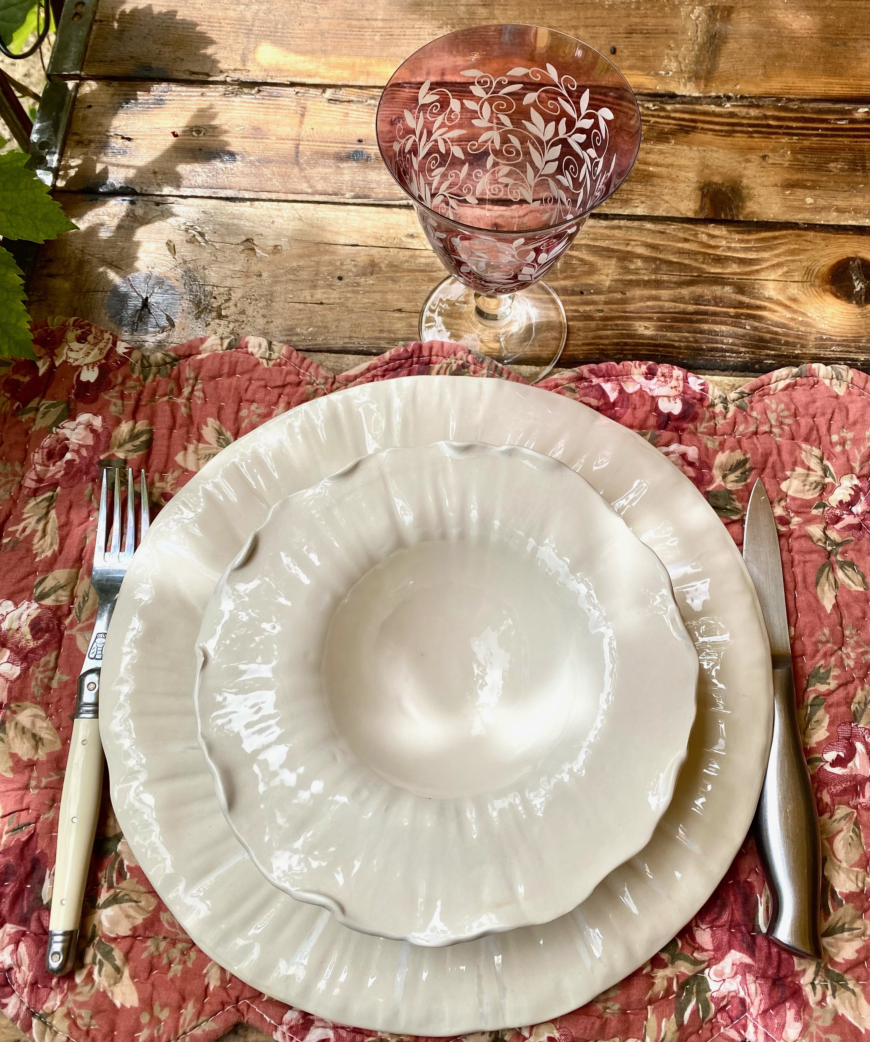 Table dressée avec assiettes creuses et plates en céramique blanche, verre rosé, nappe provençale